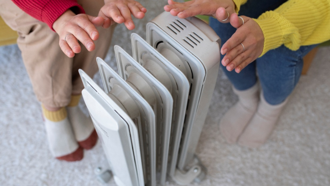 Handen verwarmen zich aan een kleine radiator - freepik.com