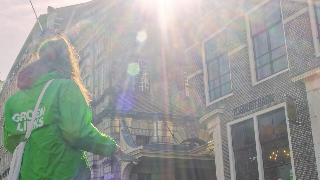 Vrouw met een GroenLinks jas deelt flyers uit